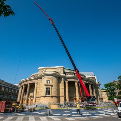 A tall red crane in front of a round historic brick buidling