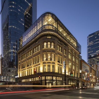 A beige historic building at night time with a modern top floor with floor to ceiling windows