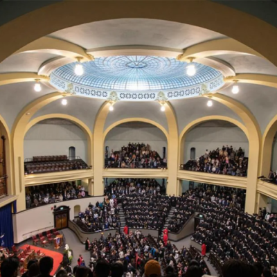 Interior of a large circular auditorium with an intricate skylight, balconies for seating, a large organ